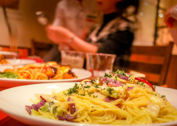 A table at an Italian restaurant, featuring pasta dishes. In the background, people dine and chat.